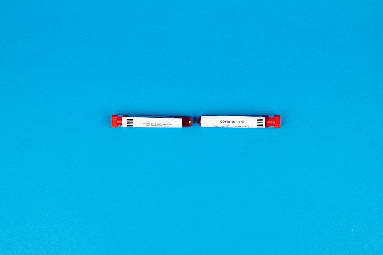 Two COVID-19 blood test vials with labels on a vibrant blue backdrop.